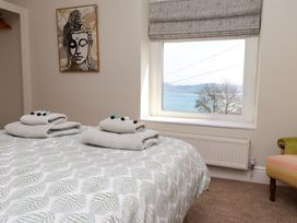 A bedroom with a bed covered in patterned bedding and folded towels on it a window showing a view of water and hills and a painting on the wall at 4 Bay View Terrace in Llandudno