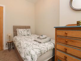 A small bedroom with a single bed patterned bed linens a wooden chest of drawers and a small round side table with a lamp at 4 Bay View Terrace in Llandudno