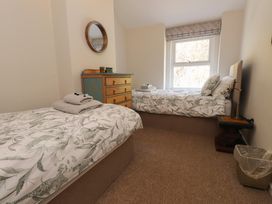 A bedroom with two single beds a wooden chest of drawers a round mirror and a window at 4 Bay View Terrace in Llandudno