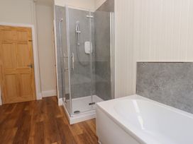 A bathroom with a wooden door a glass shower enclosure a white bathtub and wood effect flooring at 4 Bay View Terrace in Llandudno