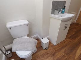 A bathroom with a toilet covered with a gray mat beside a white sink cabinet on wooden floor at 4 Bay View Terrace in Llandudno