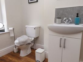 A bathroom with a toilet with a towel on it a sink with soap dispensers and a small trash bin on a wooden floor at 4 Bay View Terrace in Llandudno