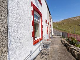 An outdoor patio area with a metal table and two chairs beside a white building with red window frames and a road and hill in the background at 4 Bay View Terrace in Llandudno