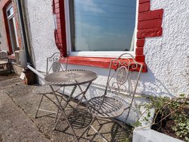 A metal table with two matching chairs on a paved area outside a building with a white wall and red window frame at 4 Bay View Terrace in Llandudno
