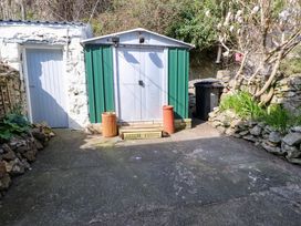 A small outdoor area with a green and white shed a white door two orange planters a black trash bin plants and a stone wall at 4 Bay View Terrace in Llandudno