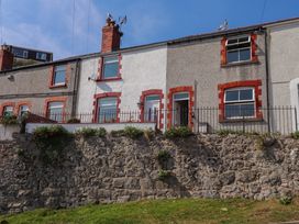 Row of terraced houses with red brick window frames and a stone retaining wall in front at 4 Bay View Terrace in Llandudno