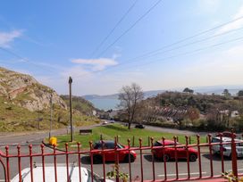 A street with parked cars near a grassy area and rocky hills with a view of the sea at 4 Bay View Terrace in Llandudno