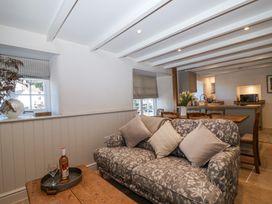 A sitting area with a patterned sofa and wooden table with a bottle and glass an open kitchen with dining table and chairs behind at Harbour View in Polperro