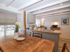 A kitchen and dining area with a wooden table, chairs, a vase of flowers, countertop with appliances, and a microwave at Harbour View in Polperro