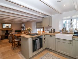 A kitchen with green cabinets and a dining table with chairs next to a living area with a fireplace at Harbour View in Polperro
