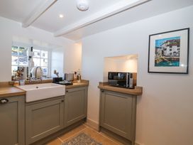 A kitchen with a ceramic sink microwave and framed artwork on the wall at Harbour View in Polperro