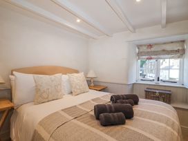 A bedroom with a double bed with pillows and folded towels on it a window with a floral blind and small tables with lamps at Harbour View in Polperro