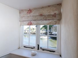 A window with floral curtains overlooking boats on water at Harbour View in Polperro