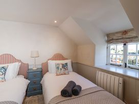A bedroom with two single beds a blue nightstand with a lamp and a window with a view at Harbour View in Polperro