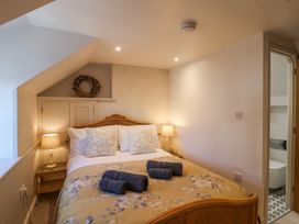 A bedroom with a double bed with floral bedding and three rolled towels two bedside tables with lamps and an open door leading to a bathroom at Harbour View in Polperro