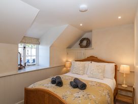 A bedroom with a wooden bed and floral bedspread two bedside tables with lamps and a window with a decorative wreath above a cupboard at Harbour View in Polperro