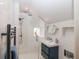 A bathroom with a glass-enclosed shower, a black towel rack with a blue towel, a sink with a dark cabinet, and a round mirror at Harbour View in Polperro
