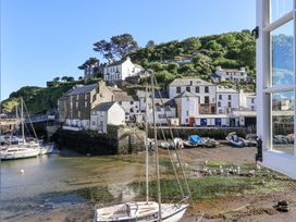 A harbor with moored boats and white buildings on a hillside viewed through an open window at Harbour View in Polperro