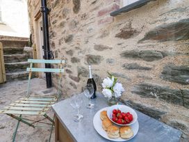 A metal chair next to a table with a bottle of wine two glasses a vase with white flowers and a plate of scones and strawberries against a stone wall at Harbour View in Polperro