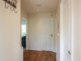 A hallway with wooden floor a white door a metal coat rack on the wall and a glimpse into a room with a sofa at Chestnut Lodge in Clunton near Clun