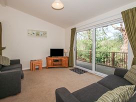 A living room with two sofas a television on a wooden stand nesting tables and a sliding glass door leading to a balcony with trees outside at Chestnut Lodge in Clunton near Clun
