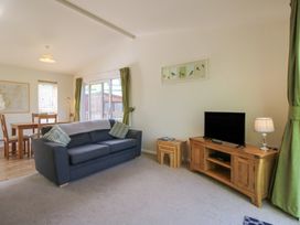 A living room with a grey sofa wooden TV cabinet and a dining table at Chestnut Lodge in Clunton near Clun