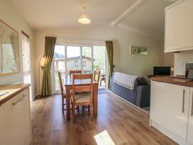 A dining area with wooden table and chairs next to a living room with a sofa and small TV at Chestnut Lodge in Clunton near Clun
