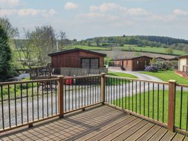 A wooden deck with railing overlooking gravel paths and wooden cabins in a rural landscape at Chestnut Lodge in Clunton near Clun