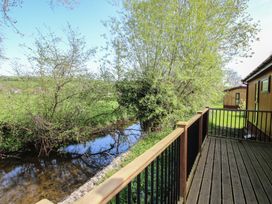 A wooden deck with railing beside a small stream and trees at Chestnut Lodge in Clunton near Clun