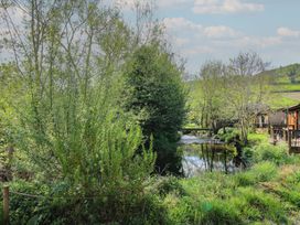 A river with trees and grass on its banks next to wooden buildings at Chestnut Lodge in Clunton near Clun