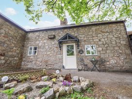 A stone cottage with a white door and two windows a small table with two chairs and a rock garden in front at Cuddfan at Swallow Cottage in Rhydtalog near Coedpoeth