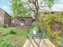 A backyard with a stone building a tree a metal table and chair with flowers on the table at Cuddfan at Swallow Cottage in Rhydtalog near Coedpoeth