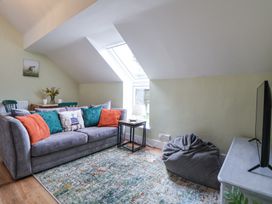 A living room with a grey sofa and colorful cushions a small table with a lamp a bean bag chair a rug a TV on a stand and a window in the ceiling at Cuddfan at Swallow Cottage in Rhydtalog near Coedpoeth
