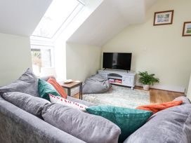 A sitting area with a grey sofa and colorful cushions a small side table a television on a cabinet a bean bag on a rug and framed pictures on the wall at Cuddfan at Swallow Cottage Rhydtalog near Coedpoeth
