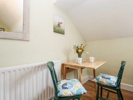 A small wooden table with two mugs and a vase of flowers with two green chairs and patterned cushions at Cuddfan at Swallow Cottage Rhydtalog near Coedpoeth