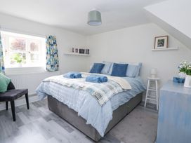 A bedroom with a double bed pillows towels and bedding a window with patterned curtains a chair and shelves with books and a framed photo at Cuddfan at Swallow Cottage in Rhydtalog near Coedpoeth
