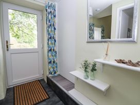 An entryway with a white door a mat patterned curtains a mirror and two shelves with glass vases and decorative items at Cuddfan at Swallow Cottage Rhydtalog near Coedpoeth
