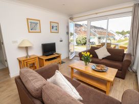 A living room with two brown sofas a wooden coffee table with flowers a TV on a wooden stand and sliding glass doors leading outside at Cape 11 near Yarmouth