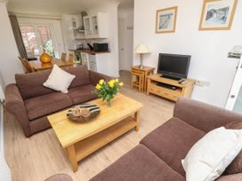 A living room with brown sofas a wooden coffee table with flowers and decorative items a TV on a wooden stand and a dining table with chairs near the kitchen at Cape 11 Near Yarmouth