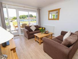 A living room with two brown sofas, a wooden coffee table with flowers, a mirror on the wall, and glass doors leading to an outdoor seating area at Cape 11 Near Yarmouth