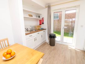 A kitchen with white cabinets a wooden table with oranges a trash bin and glass doors opening to a garden at Cape 11 Near Yarmouth
