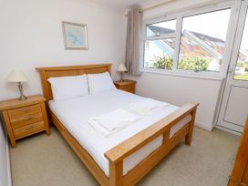 A bedroom with a wooden bed frame white bedding two wooden bedside tables with lamps a window and a door at Cape 11 Near Yarmouth