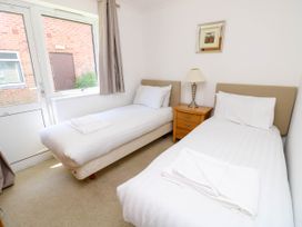A bedroom with two single beds a wooden nightstand with a lamp a window and a door at Cape 11 Near Yarmouth
