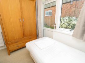 A bedroom with a wooden wardrobe a white bed and a door leading outside with a window showing white flowers outside at Cape 11 Near Yarmouth