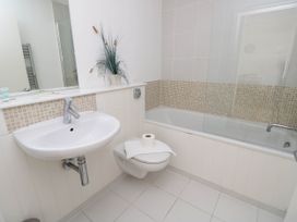 A bathroom with a wall-mounted sink toilet and bathtub with tiled walls and a plant on the counter at Cape 11 Near Yarmouth