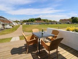 An outdoor patio with a table and four chairs with a bottle and glasses overlooking a grassy area with small houses at Cape 11 Near Yarmouth