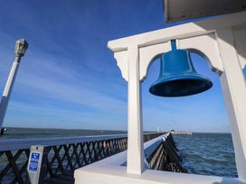 A wooden pier extending into the sea with a blue bell hanging from a white wooden frame near the start of the pier at Cape 11 Near Yarmouth