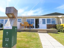 The exterior of a single-story cottage with a wooden deck patio and outdoor table and chairs at Cape 12 Near Yarmouth