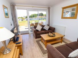 A living room with brown sofas a wooden coffee table a television on a wooden cabinet and a sliding glass door leading to an outdoor area with chairs and a table at Cape 12 Near Yarmouth