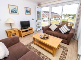 A living room with brown sofas a wooden coffee table a television on a wooden stand and sliding glass doors leading outside at Cape 12 Near Yarmouth